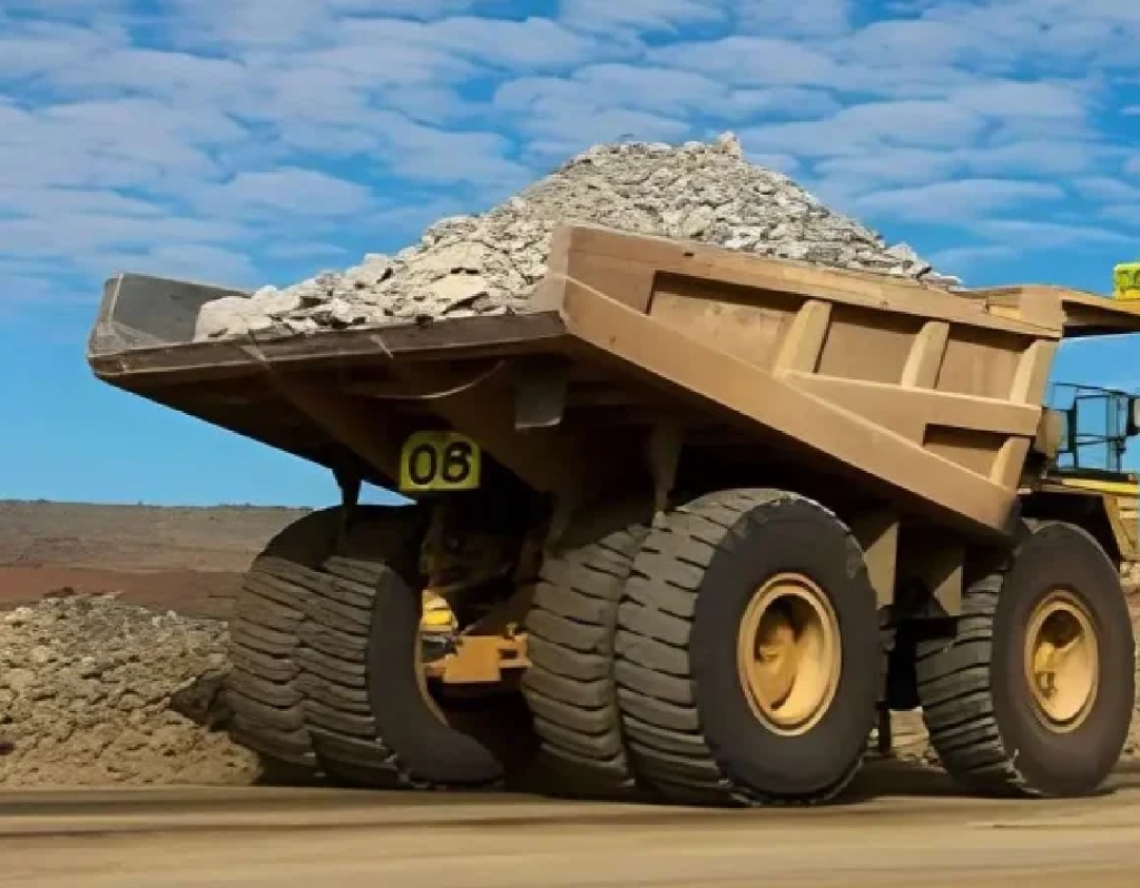 A heavy-duty yellow mining dump truck with oversized tires transporting crushed rock at an open mining site.